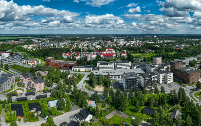Viistoilmakuva Seinäjoen keskustasta. Kuvassa erottuu rakennuksia, vehreyttä , teitä ja poutapilvinen taivas.