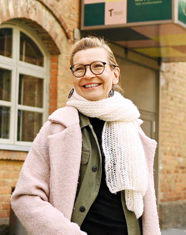 A woman is standing and smiling in front of a red brick building.