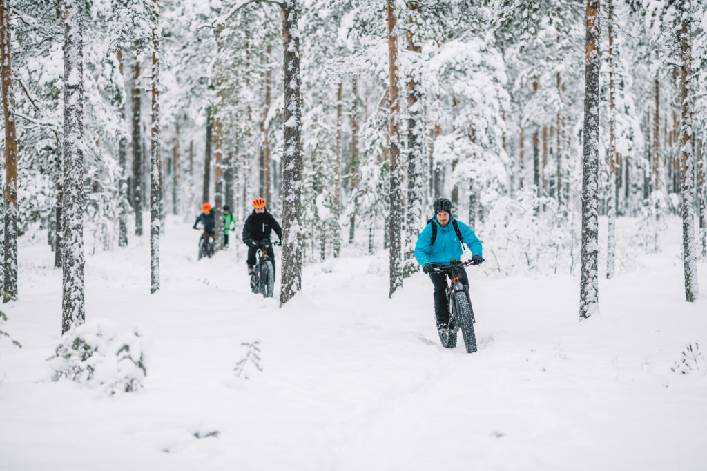 Neljä maastopyöräilijää lumisella metsäpolulla.