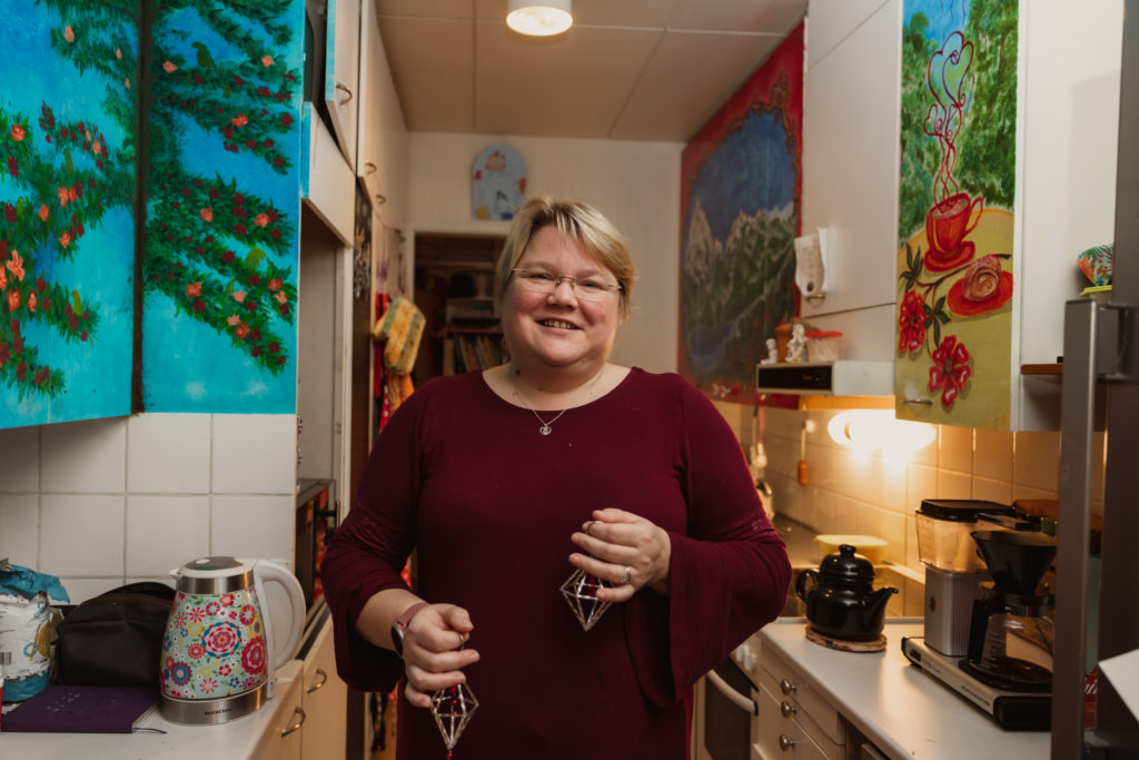 Nainen seisoo värikkäässä keittiössä joulukoristeet käsissään.