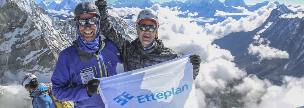 Kaksi miestä on valloittanut vuoren huipun ja he hymyssä suin pitelevät käsissään valkoista lippua, jossa lukee Etteplan.