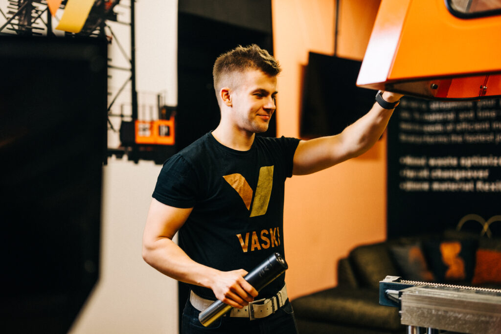 Mies mustassa Vaski-t-paidassa jonkinlaisen laitteen äärellä.