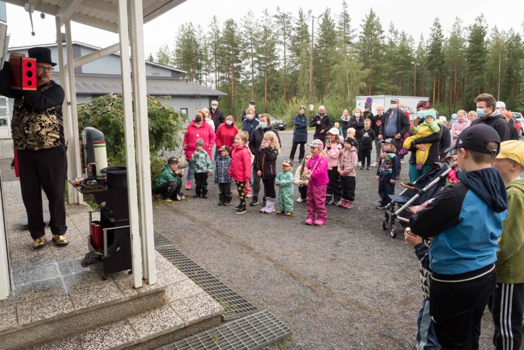 Taikuri esiintyy katoksen alla. Ihmisjoukko seisoskelee yleisönä.