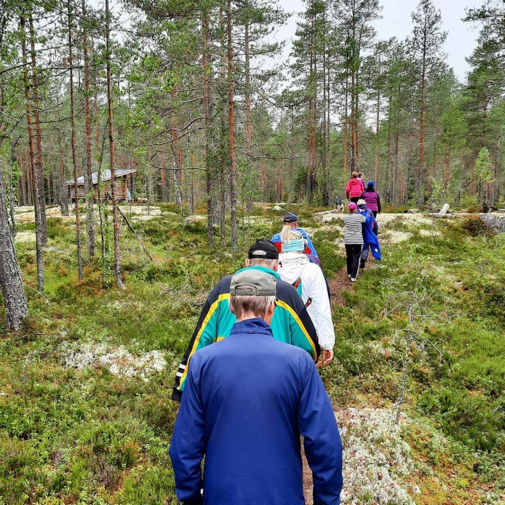 Ihmiset kävelevät peräkkäin luontopolulla metsämaisemissa.