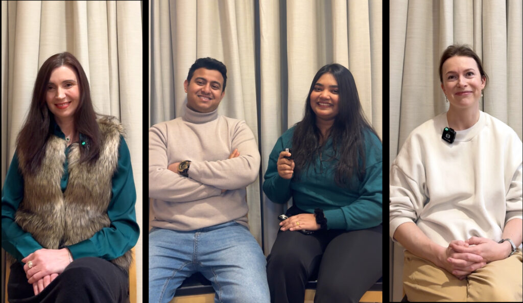 Neljä aikuista ihmistä istuvat verhon edessä tuoleilla.