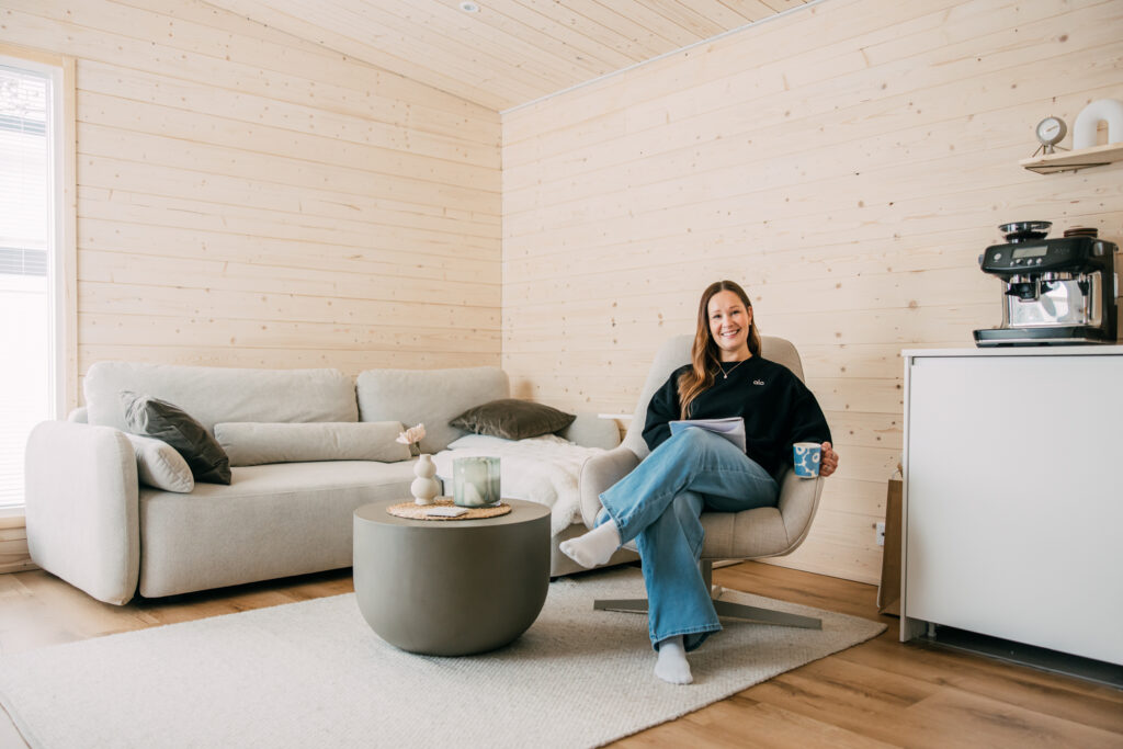 Nainen istuu vaaleasävyisen olohuoneen nojatuolissa.