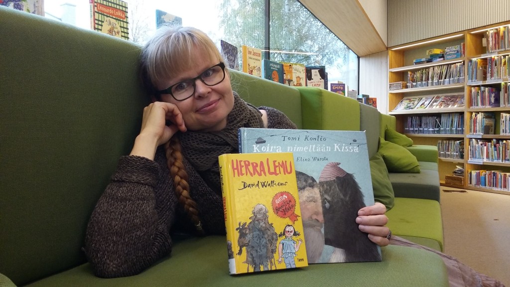 Mervi Heikkilä istuu ja esittelee kahta lukupiiriin valittua kirjaa Apila-kirjaston lastenosastolla.