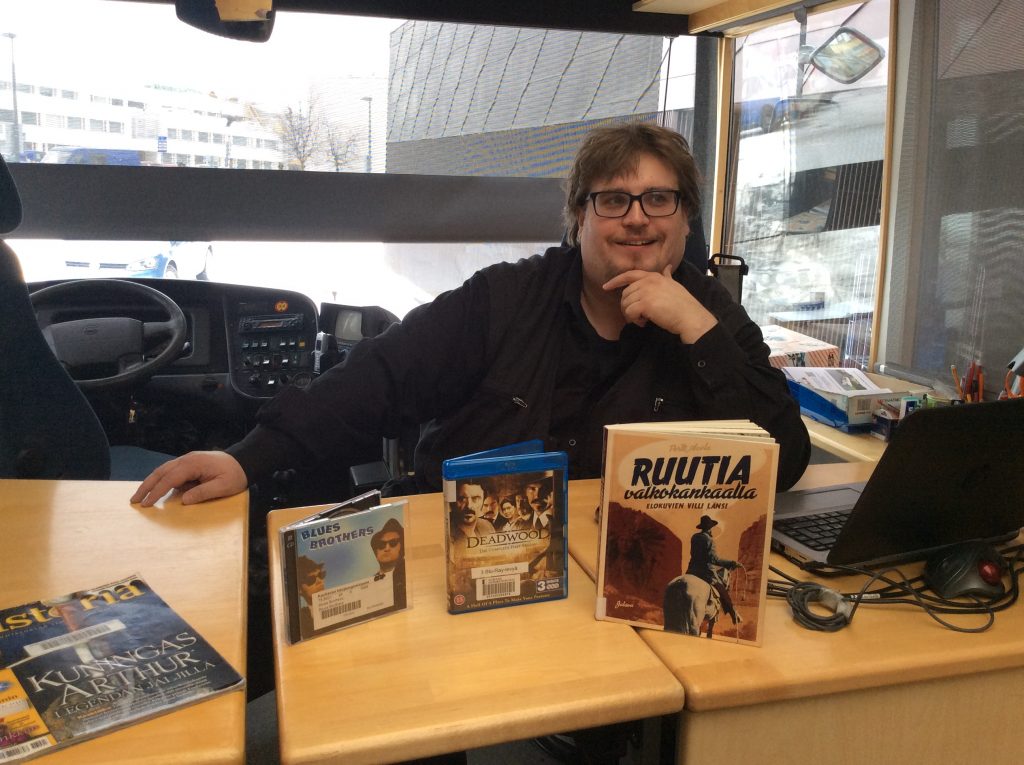 Jussi Haapala istuu kirjastoauto Ykässä ja pöydällä ovat hänen suosikkikirjat.