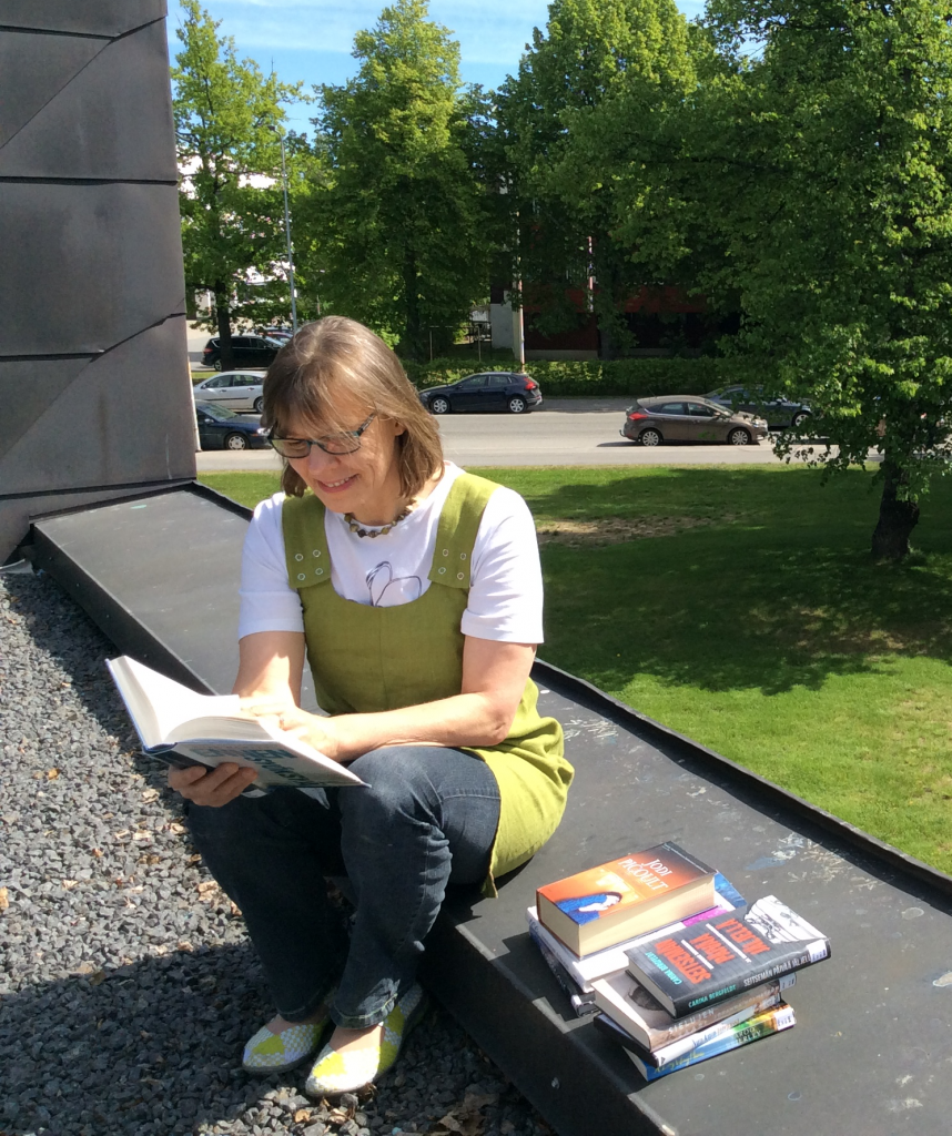 Sirpa Rintamäki lukemassa kirjaa ulkona.