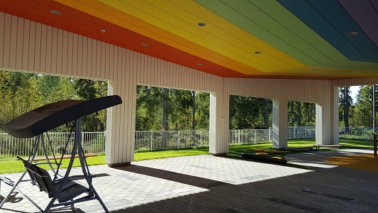 Takapihan katettu leikkialue, jonka sisäkatto on maalattu sateenkaaren väreillä.
