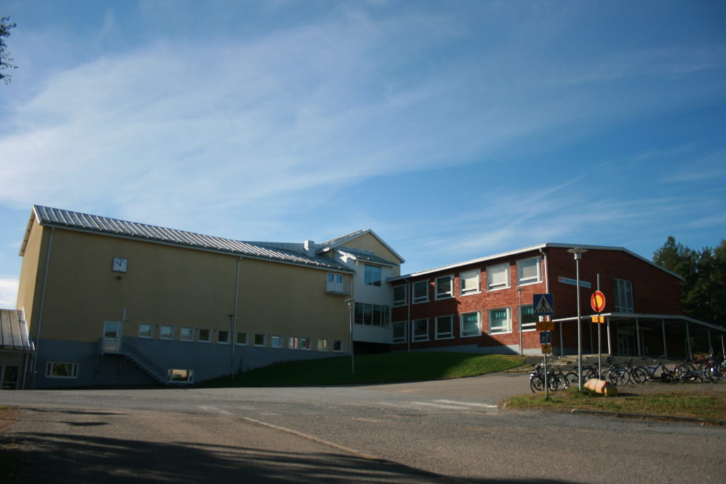 Mäen päälle rakennettu Valkiavuoren koulu kesällä kuvattuna. Vasemmalla puolella on korkea keltainen osa ja oikealla punainen, kerroksen matalampi tiilinen osa koulua. rakennukset ovat kiinni toisissaan.