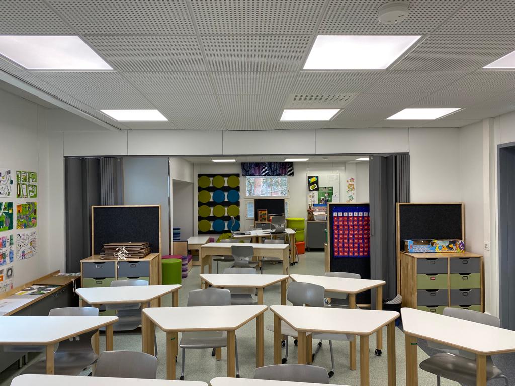 Luokkahuone, jossa valoisia pulpetteja tuoleineen ja säilytyslaatikosto oikeassa reunassa. Katossa on upotettuna kuusi suorakaiteen muotoista valaisinlaattaa.