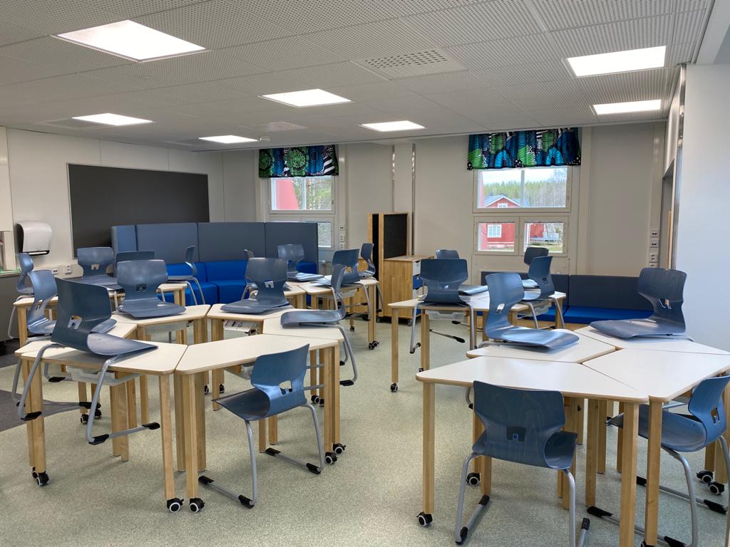Luokkahuone, jossa sinisiä oppilastuoleja ja valkoisia pulpetteja ympyrän muodossa ja ryhminä.