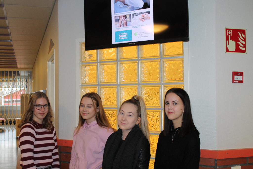 Neljä oppilasta seisoo vierekkäin info-TV:n alla kasvot kameraan päin.
