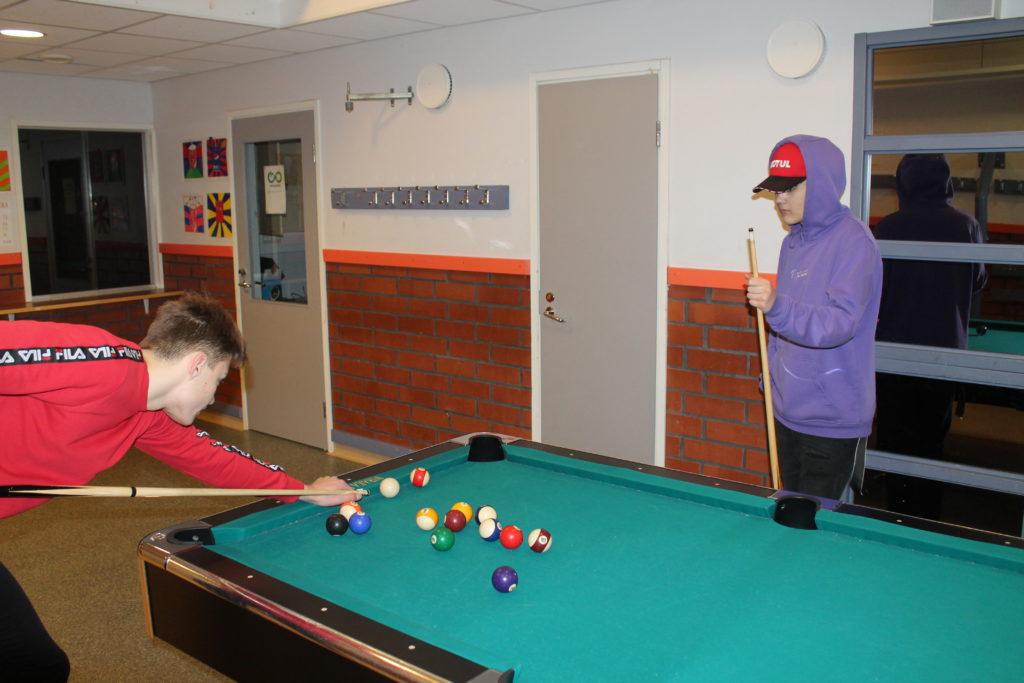 Kaksi oppilasta pelaa biljardia koulun sisätiloissa.