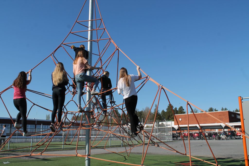 Kuusi oppilasta kiipeilee vaijerikiipeilytelineessä koulun pihalla.