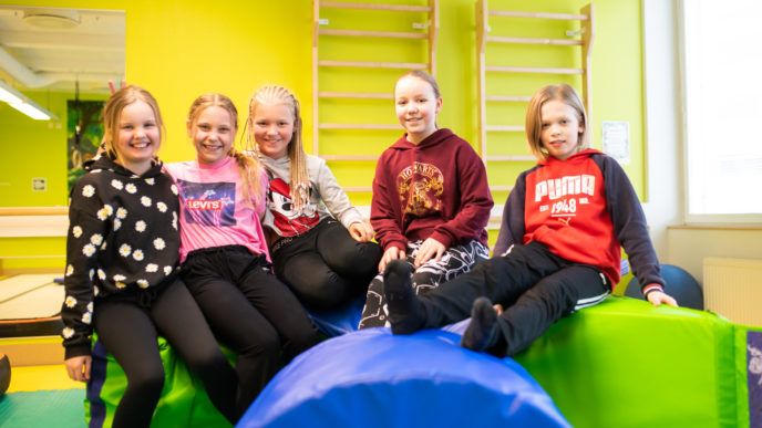 Lapsia istumassa liikuntasalissa patojen päällä.