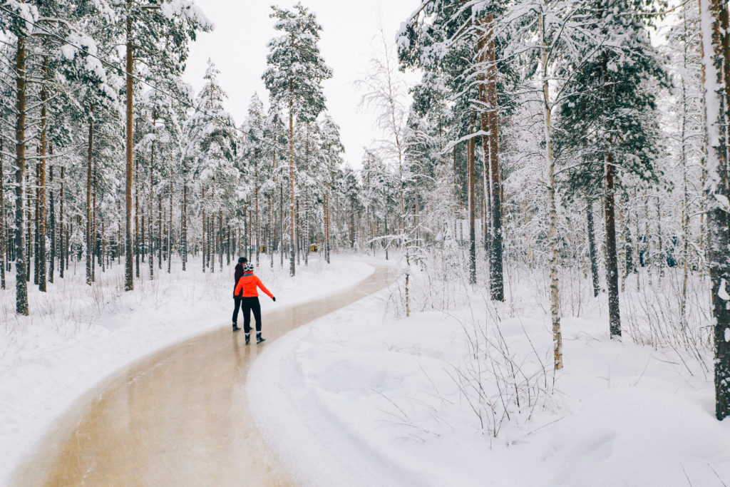 Kuvassa kaksi henkilöä luistelee metsässä olevalla retkiluisteluradalla.