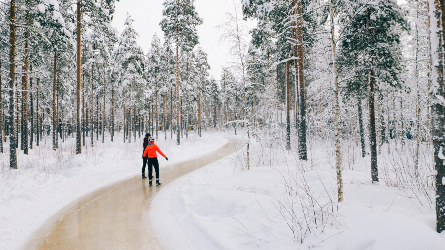 Kuvassa kaksi henkilöä luistelee metsässä olevalla retkiluisteluradalla.