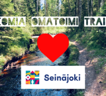 Kuvassa puro, polku ja metsää. Edessä teksti Komia omatoimi trail, sydän ja Seinäjoki-logo.