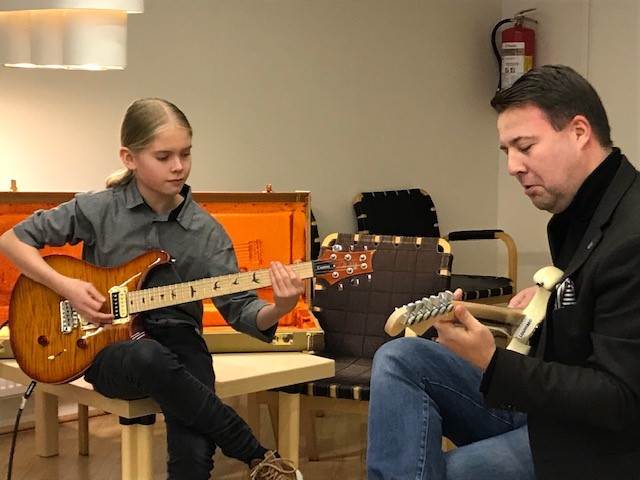 Kaksi kitaransoittajaa istuvat vastakkain. Toinen soittaja on nuori poika.