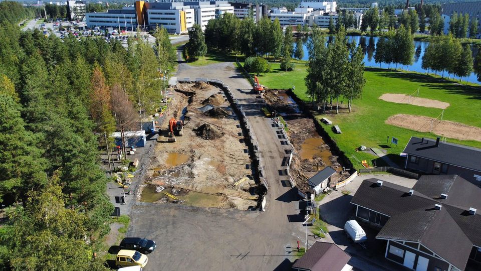 Kuvassa Kyrkösjärven uimarannan parkkipaikka missä kaksi kaivinkonetta kunnostamassa aluetta. Ympärillä metsää, uimarannan rakennuksia, kaksi rantalentopallokenttää ja taustalla sairaala.