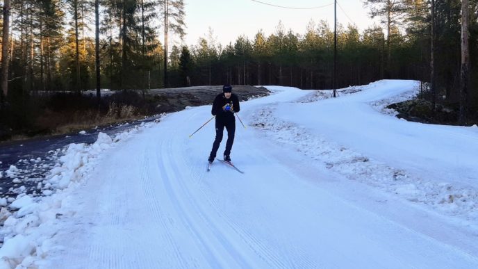 Kuvassa hiihtäjä mustissa vaatteissa ensilumenladulla. Ympärillä metsää ja lunta vain ladulla.