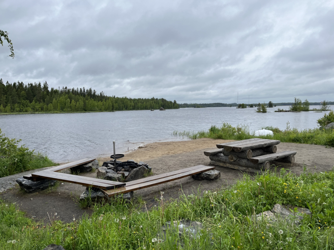 Kuvassa on rakennettuna grillipaikka ja istuinpenkki ja pöydät järven rannalle.