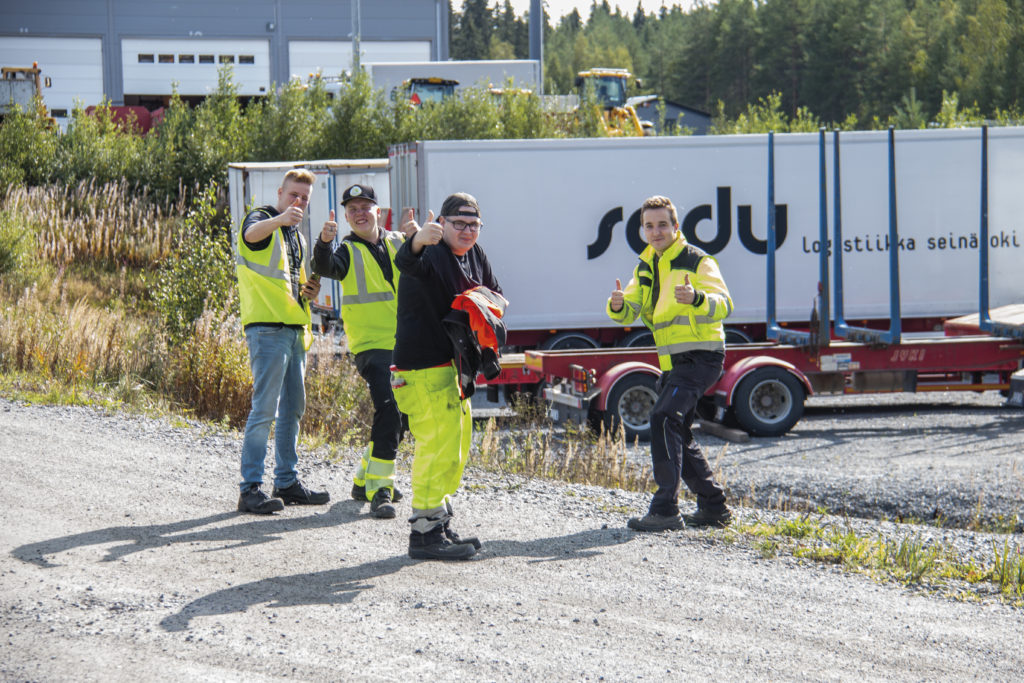 Neljä opiskelijaa peukuttavat kameralle keltaiset huomiovaatteet yllään.