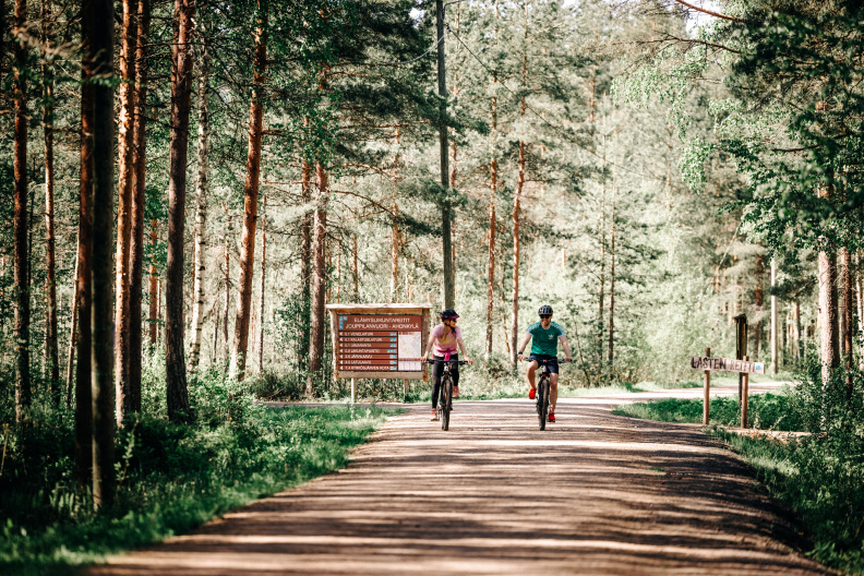 Kuvassa kaksi pyöräilijää kuntoradalla. Taustalla reittiopasteita ja metsää.
