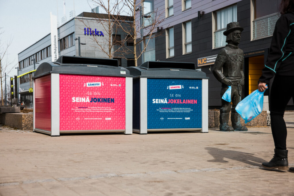 Kaksi roskalaatikkoa teippailtu värikkäästi: toinen sinisellä ja toinen pinkillä.
