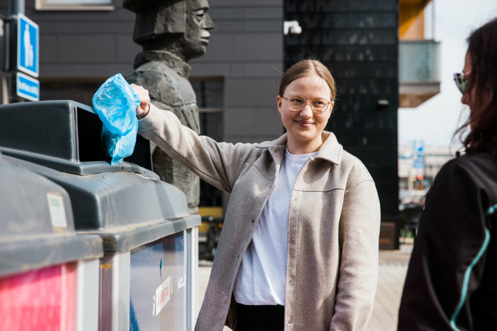 Nuori nainen laittaa sinistä roskapussia roskikseen.