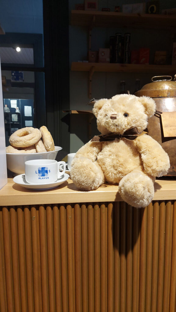 Lelunalle istuu tasolla, vieressään kahvikuppi Lotta Svärd logolla.