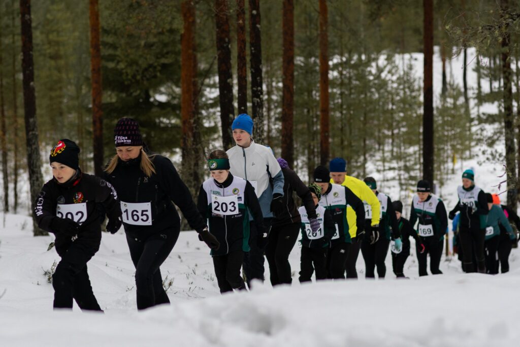 Henkilöitä jonossa juoksemassa lumista polkua metsässä.