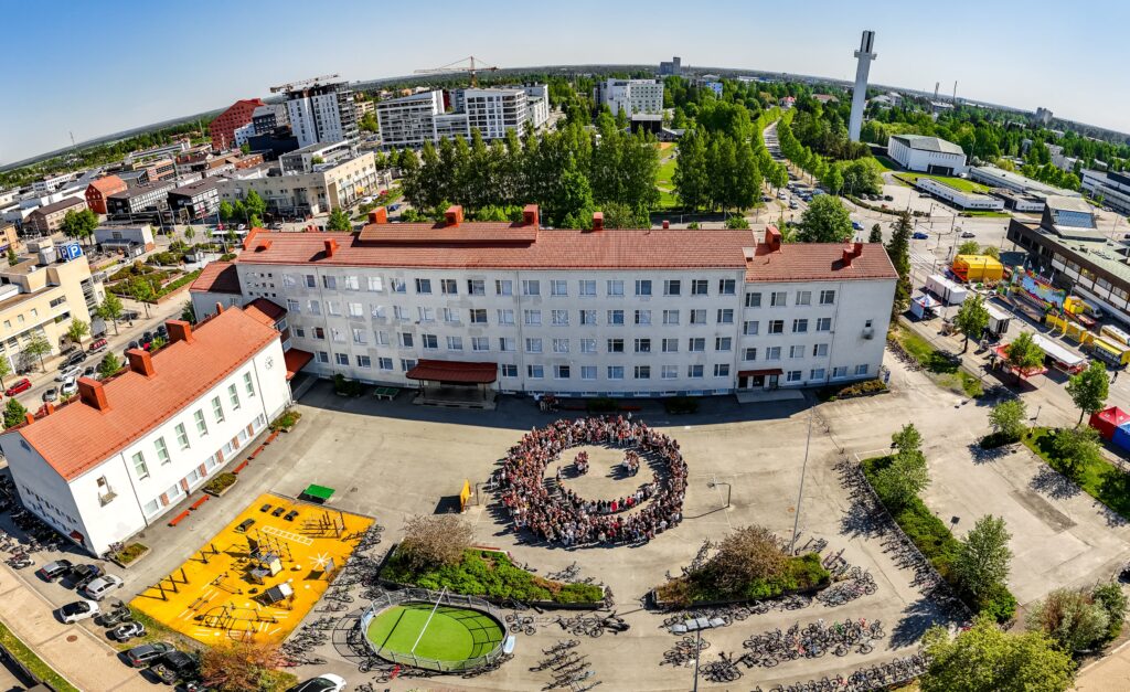 Aurinkoinen kuva Lyseonpihasta. Kaikista Lyseon oppilaista on muodostettu pihaan hymäri.