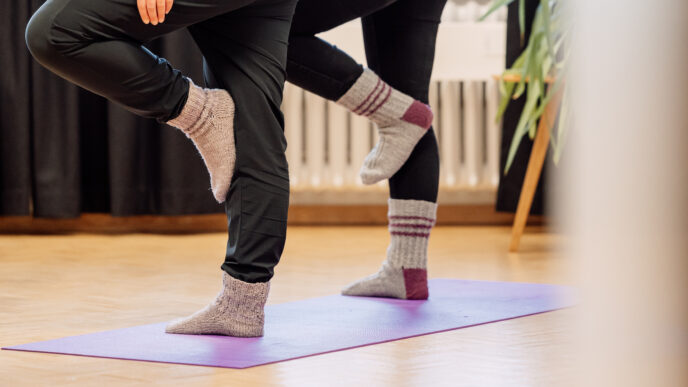 kaksi henkilöä seisoo villasukissa, toinen jalka vastan polvea