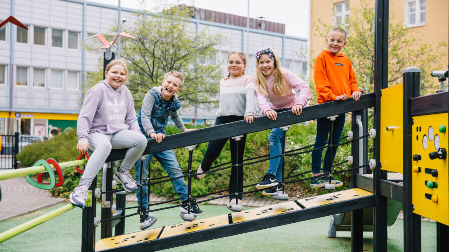 Viisi lasta nauraa kiipeilytelineen sillalla.