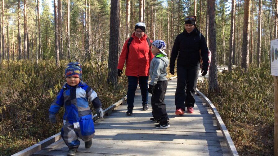 Kaksi aikuista ja kaksi lasta kävelee metsässä olevalla lankkupolulla.
