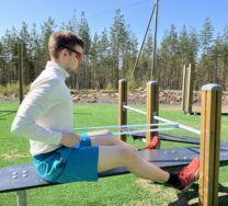 Henkilö vetää soutuasennossa kuminauhaa ulkokuntoilutelineellä.