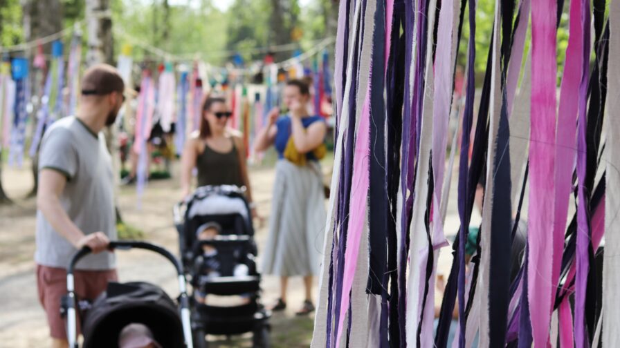Kuvassa ihmisiä ja lastenrattaita festivaalialueella. Alueella värikkäitä koristeita.