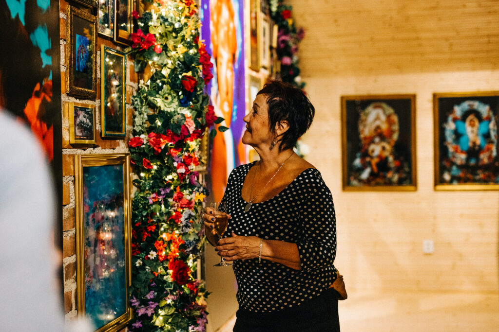 Henkilö katselee seinälle ripustettuja taideteoksia. Kädessä on viinilasi.