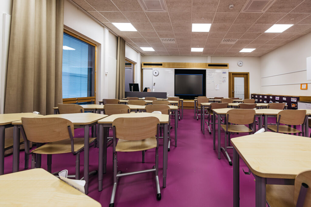 Kärjen koulun luokkahuone. Luokassa punainen lattia ja puiset kalusteet.