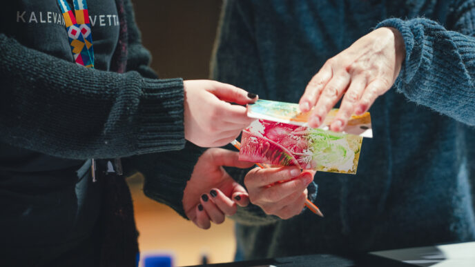 Kuvassa näkyy kahden ihmisen kädet, jotka pitelevät yhdessä värikästä korttia.