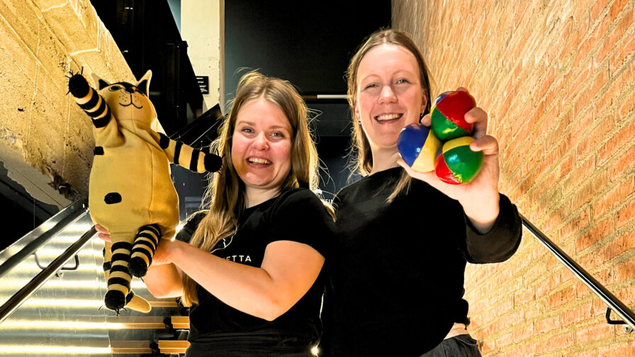 kuvassa kaksi henkilöä seisomassa vierekkäin portailla. Toisella on kädessään kissan näköinen käsinukke ja toisella kolme jongleerauspalloa.