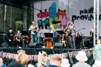 Kuvassa orkesteri esiintyy esiintymislavalla, jonka edustalla on joukko ihimisä.