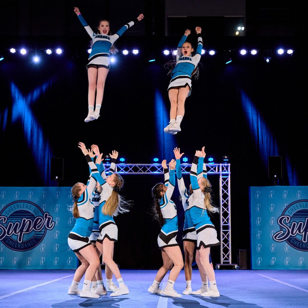 Cheerleadereita esiintymässä lavalla. Kaksi joukkoa ottaa kahta henkilöä alas ilmasta.