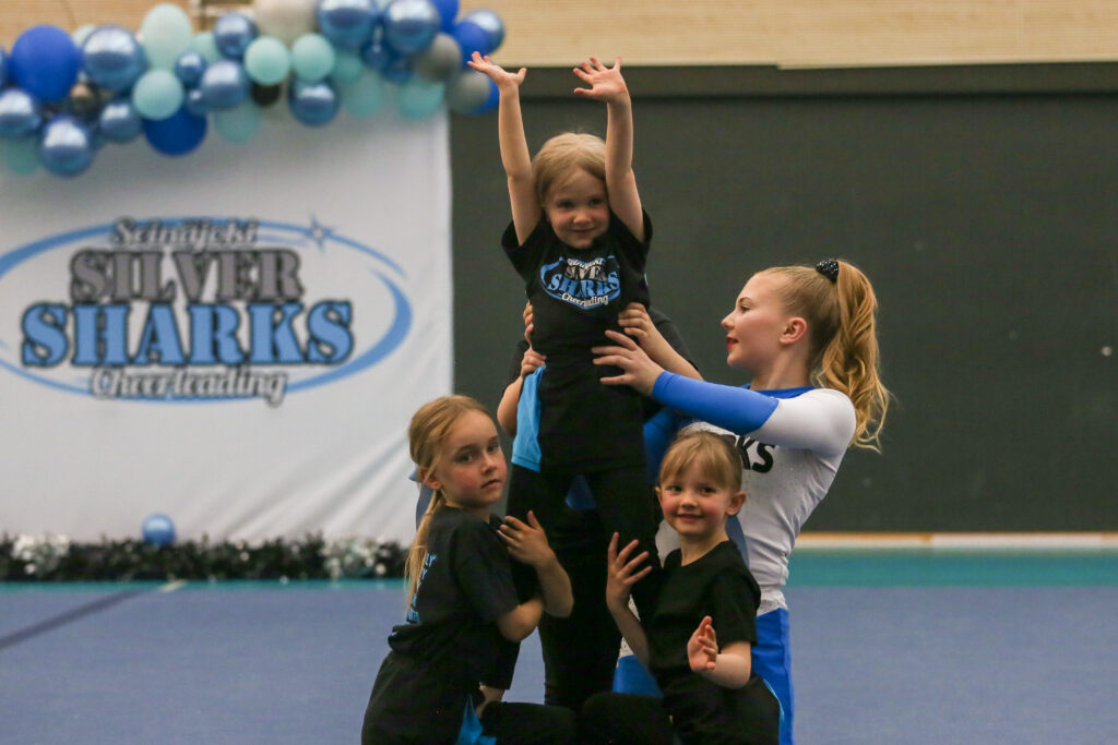 Cheerleader lapset tekemässä nostoa jota aikuinen avustaa.