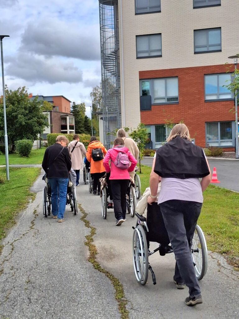 Ikääntyneitä ulkoilemassa kerrostalon edessä kulkevalla pihatiellä.