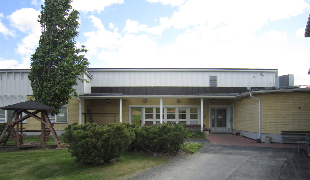 Pääsisäänkäynti, rakennus on keltatiilinen. 