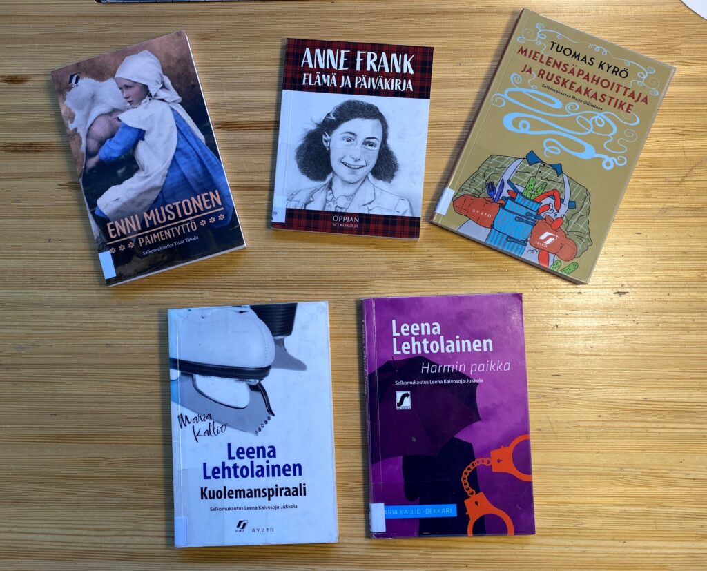 Pöydällä ovat selkomukautukset seuraavista kirjoista: Enni Mustonen: Paimentyttö, Anne Frankin päiväkirja, Tuomas Kyrö: Mielensäpahoittaja ja ruskeakastike sekä Leena Lehtolainen: Kuolemanspiraali ja Harmin paikka.